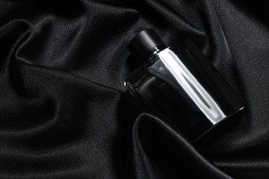 Luxury men's perfume in bottle on black satin fabric, top view. Space for text