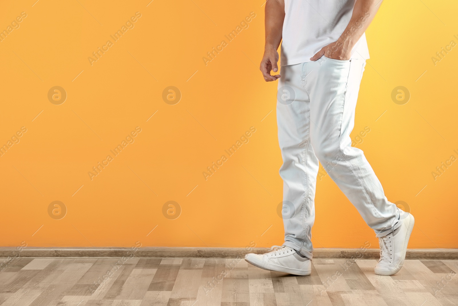 Photo of Young man in stylish jeans near color wall with space for text, focus on legs