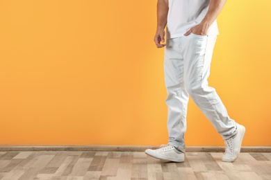 Photo of Young man in stylish jeans near color wall with space for text, focus on legs