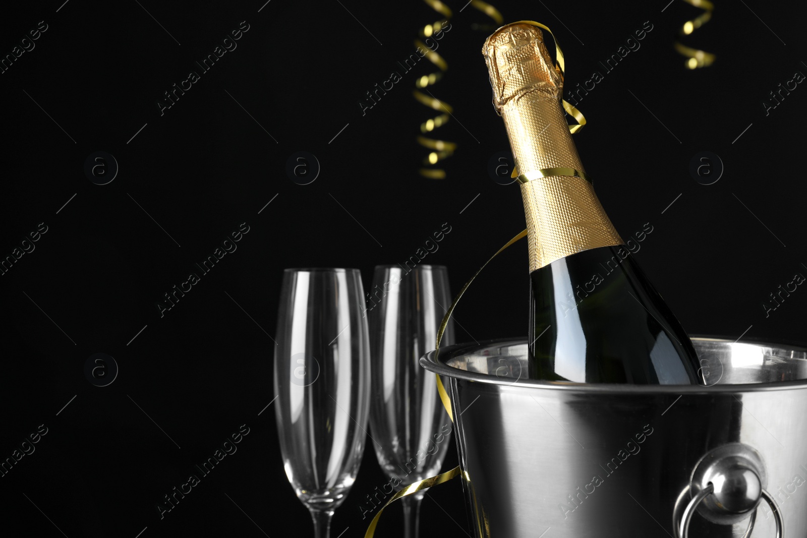 Photo of Happy New Year! Bottle of sparkling wine in bucket and glasses on black background, space for text
