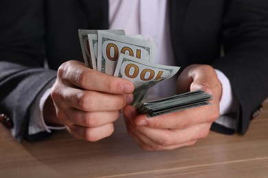 Photo of Money exchange. Man counting dollar banknotes at wooden table, closeup