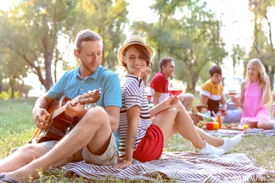 Photo of Young man playing guitar for his girlfriend in park. Summer picnic