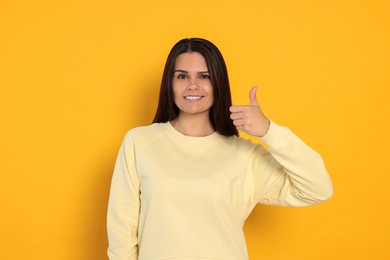 Young woman showing thumb up on orange background