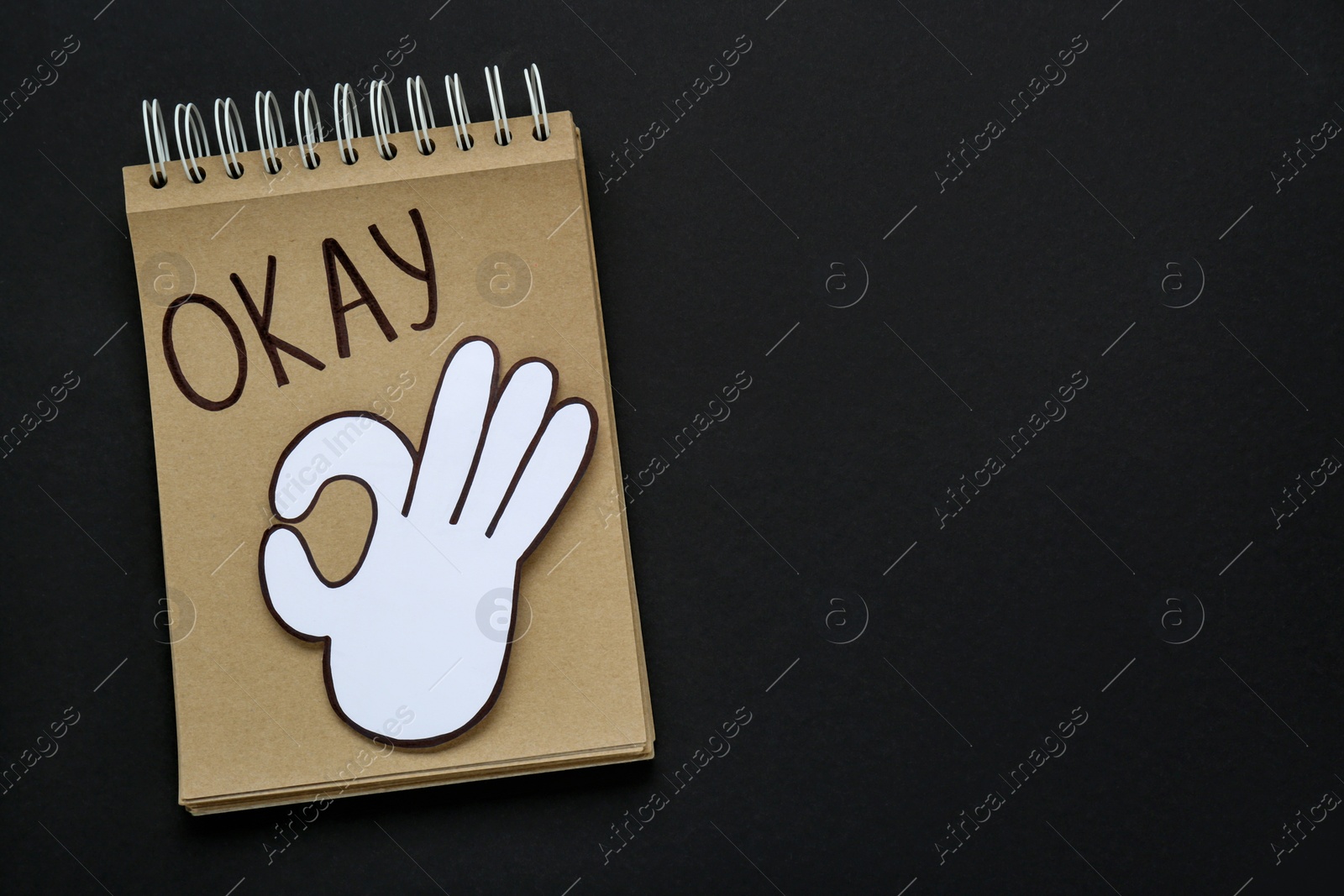 Photo of Notepad with word Okay and paper cutout of hand (OK gesture) on black background, top view. Space for text