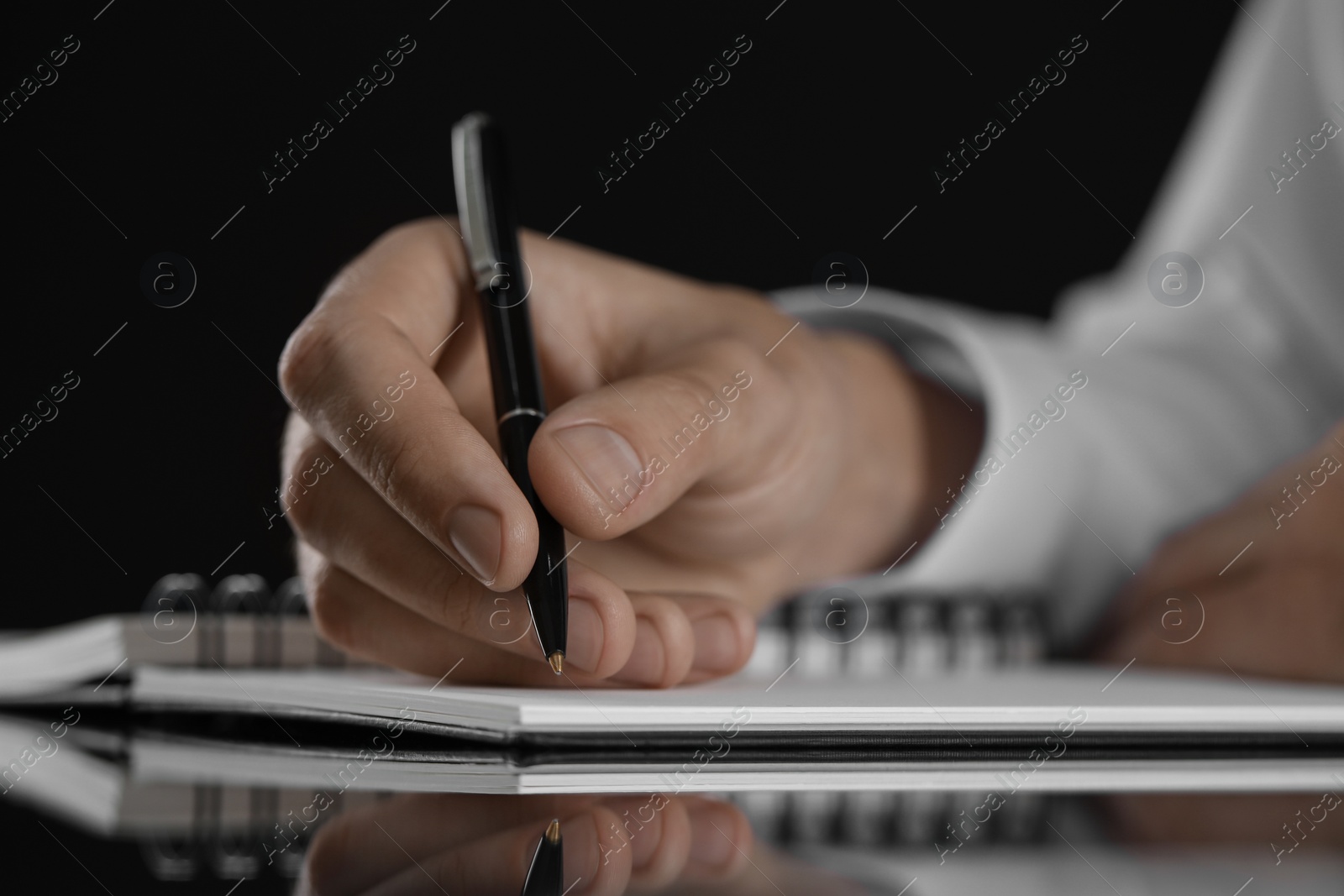 Photo of Man writing in notebook at black table, closeup