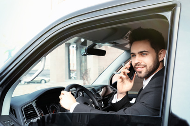 Handsome young man talking on smartphone while driving his car