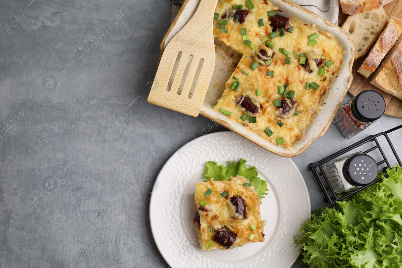 Photo of Tasty sausage casserole with green onions served on grey table, flat lay. Space for text