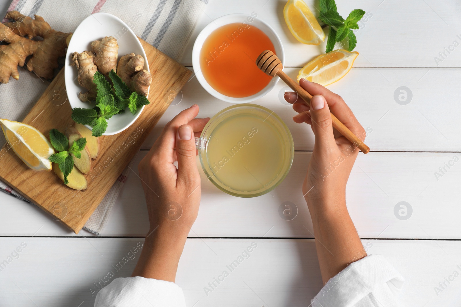 Photo of Woman drinking delicious ginger tea with honey at white wooden table, top view