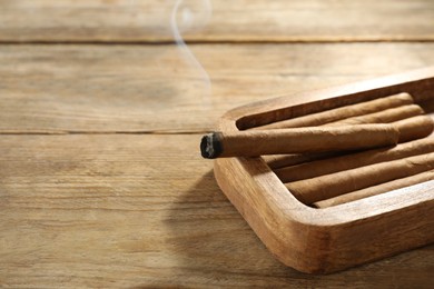 Photo of Many cigars in box on wooden table, space for text