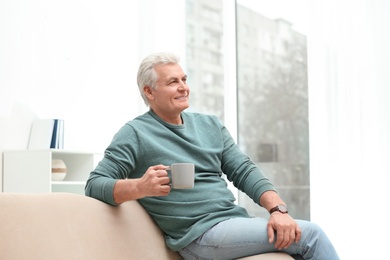 Portrait of mature man with cup of drink on sofa indoors