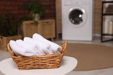 Photo of Wicker basket with folded towels on white table in laundry room. Space for text