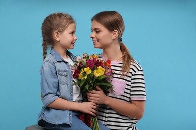 Little daughter congratulating her mom with flowers on light blue background. Happy Mother's Day