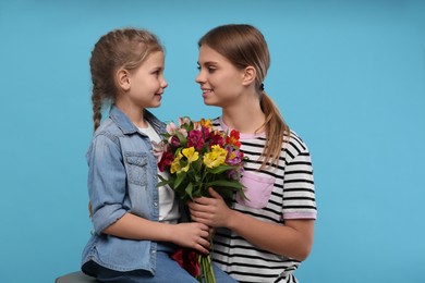 Photo of Little daughter congratulating her mom with flowers on light blue background. Happy Mother's Day