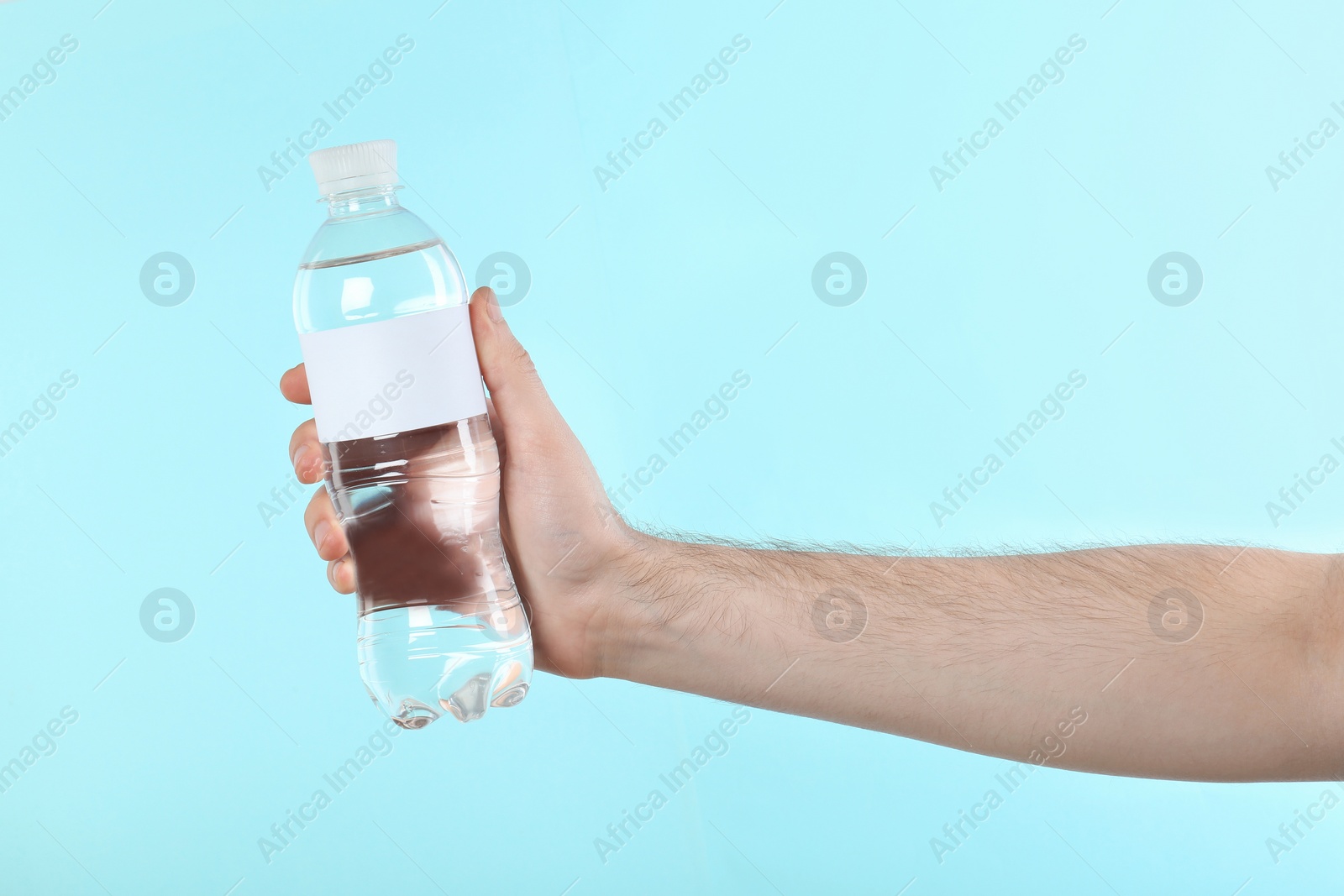 Photo of Man holding plastic bottle of pure water with blank tag on color background