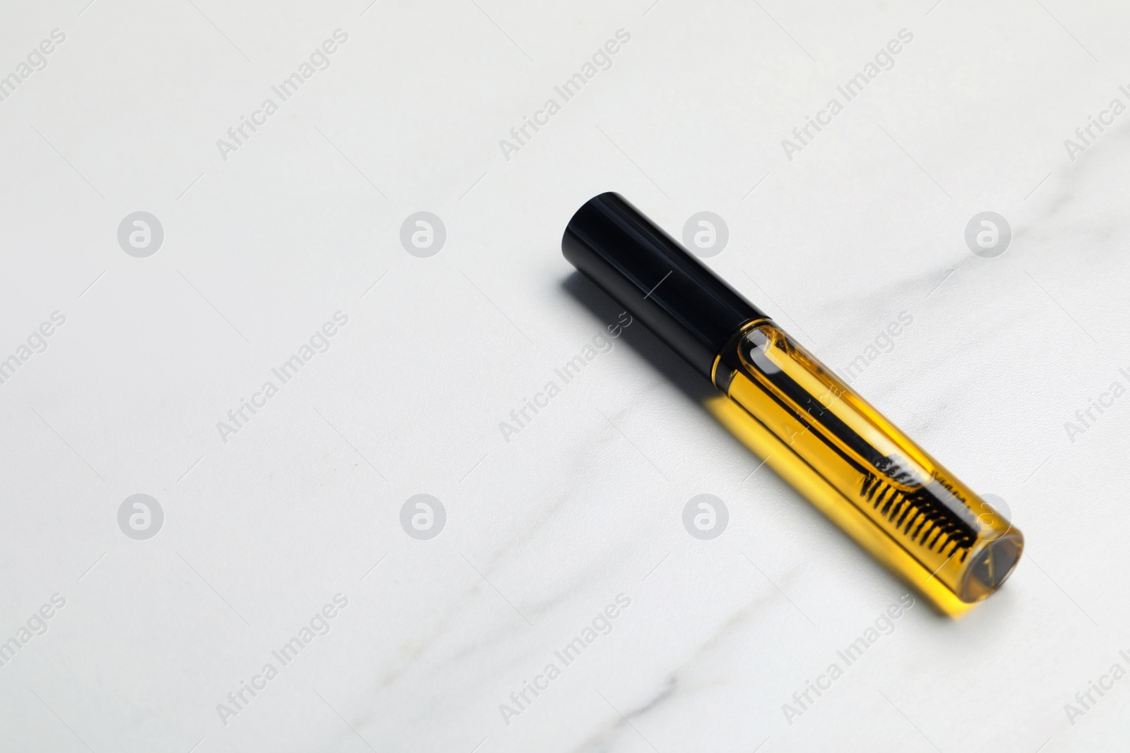 Photo of Tube of eyelash oil on white marble table. Space for text