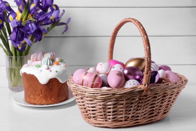 Photo of Wicker basket with festively decorated eggs, Easter cake and iris flowers on white table