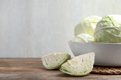 Photo of Fresh whole and cut cabbages in bowl on wooden table. Space for text