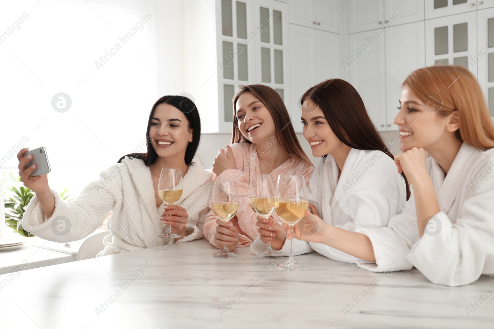 Photo of Beautiful young ladies with wine taking selfie in kitchen at pamper party. Women's Day