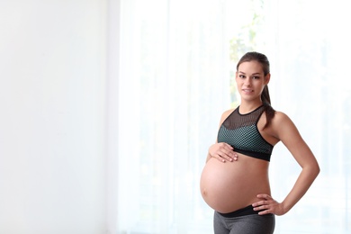 Photo of Young pregnant woman in fitness clothes at home. Space for text