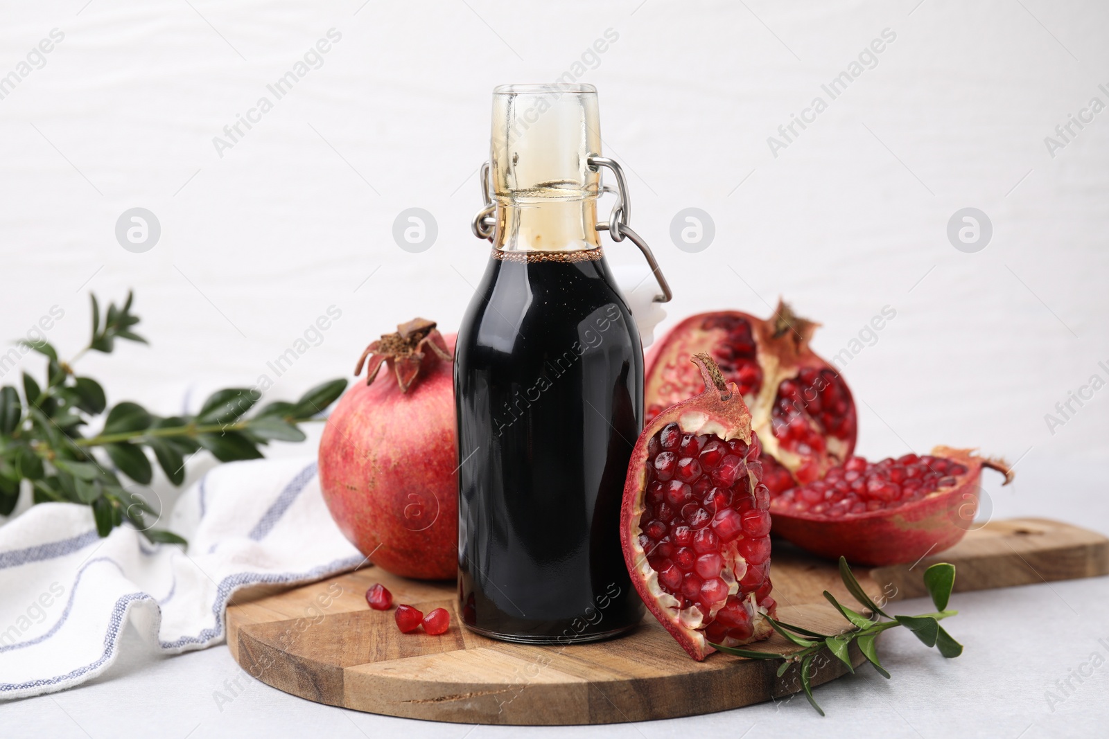 Photo of Tasty pomegranate sauce in bottle, branches and fruits on light table, closeup