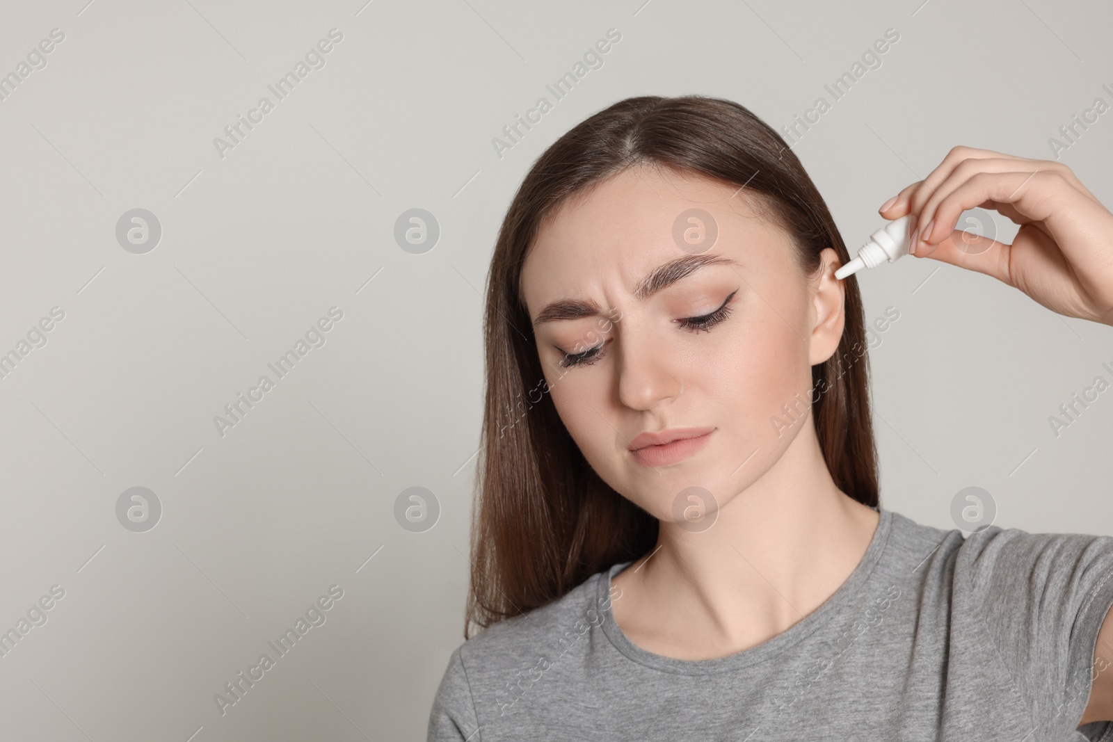 Photo of Young woman using ear drops on light grey background. Space for text