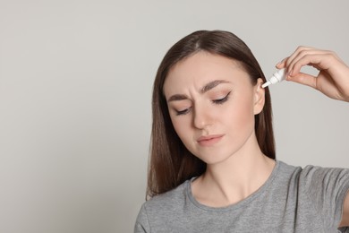 Young woman using ear drops on light grey background. Space for text