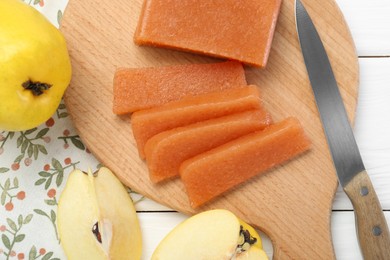 Tasty sweet quince paste, fresh fruits and knife on white wooden table, flat lay