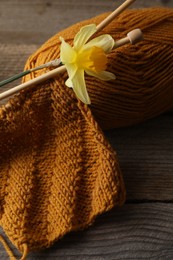 Photo of Soft orange knitting, daffodil flower, yarn and needles on wooden table, closeup