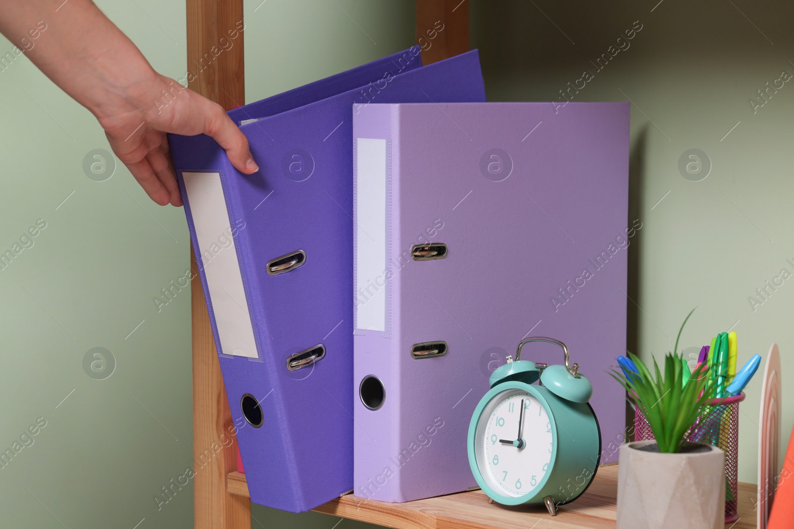 Photo of Woman taking binder office folder from shelving unit indoors, closeup