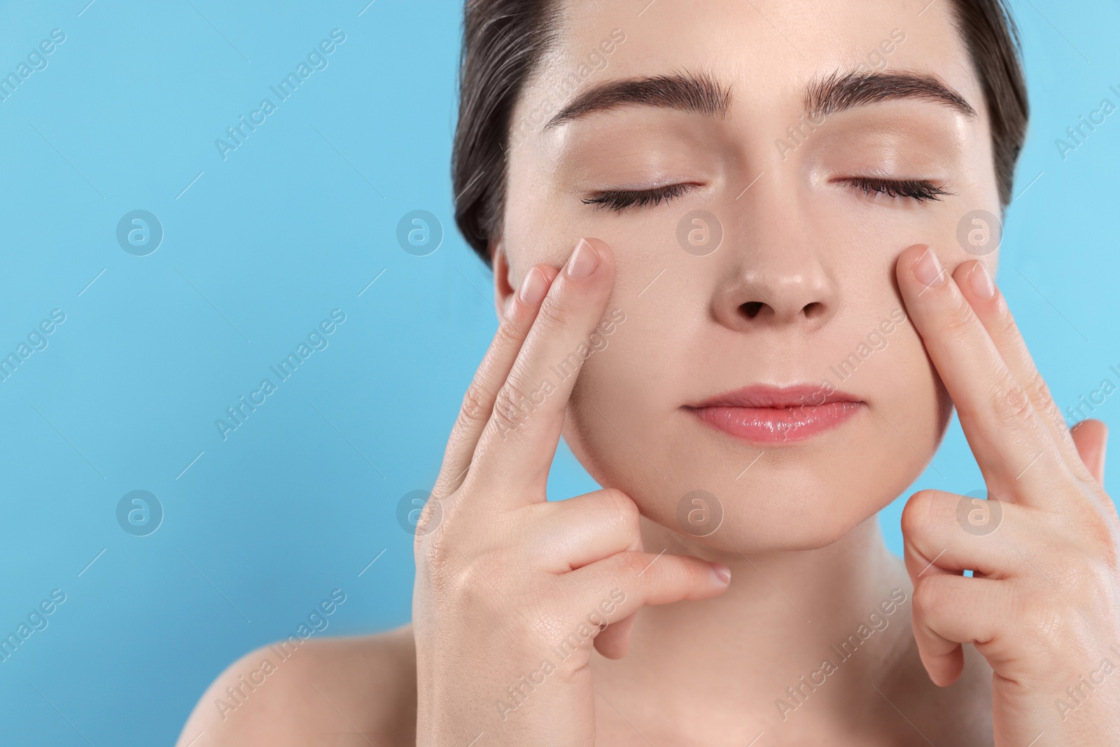 Photo of Young woman massaging her face on turquoise background. Space for text