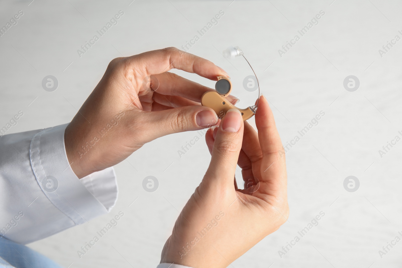 Photo of Woman putting battery into hearing aid on light background, closeup