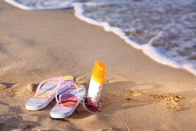 Photo of Flip flops and beach accessories on sand near sea. Space for text