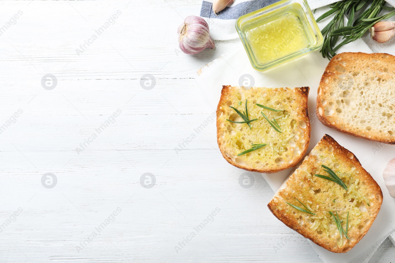 Photo of Slices of toasted bread with garlic and herb on white wooden table, flat lay. Space for text