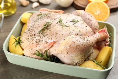 Raw chicken with potatoes and rosemary on wooden table, closeup