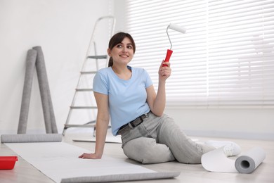 Photo of Woman with roller and wallpaper in room