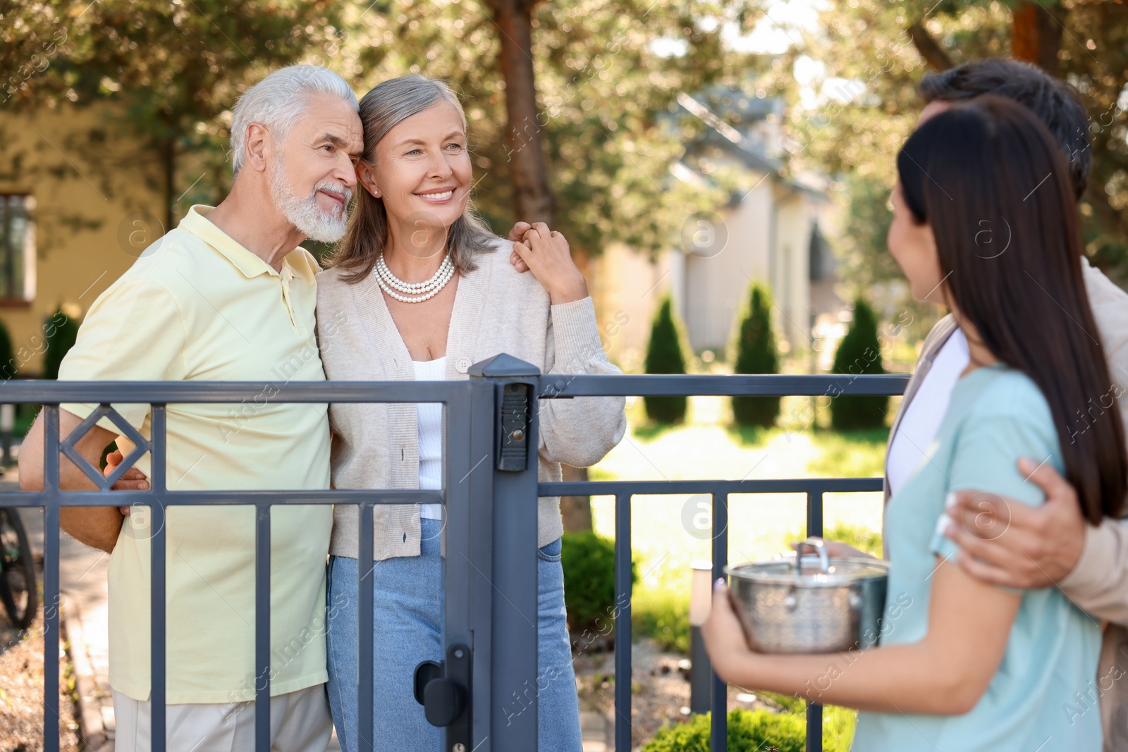 Photo of Friendly relationship with neighbours. Young family talking to elderly couple near fence outdoors