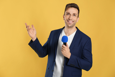 Young male journalist with microphone on yellow background