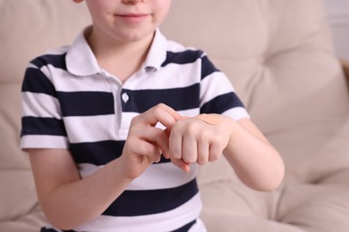 Little boy putting sticking plaster onto hand on sofa, closeup