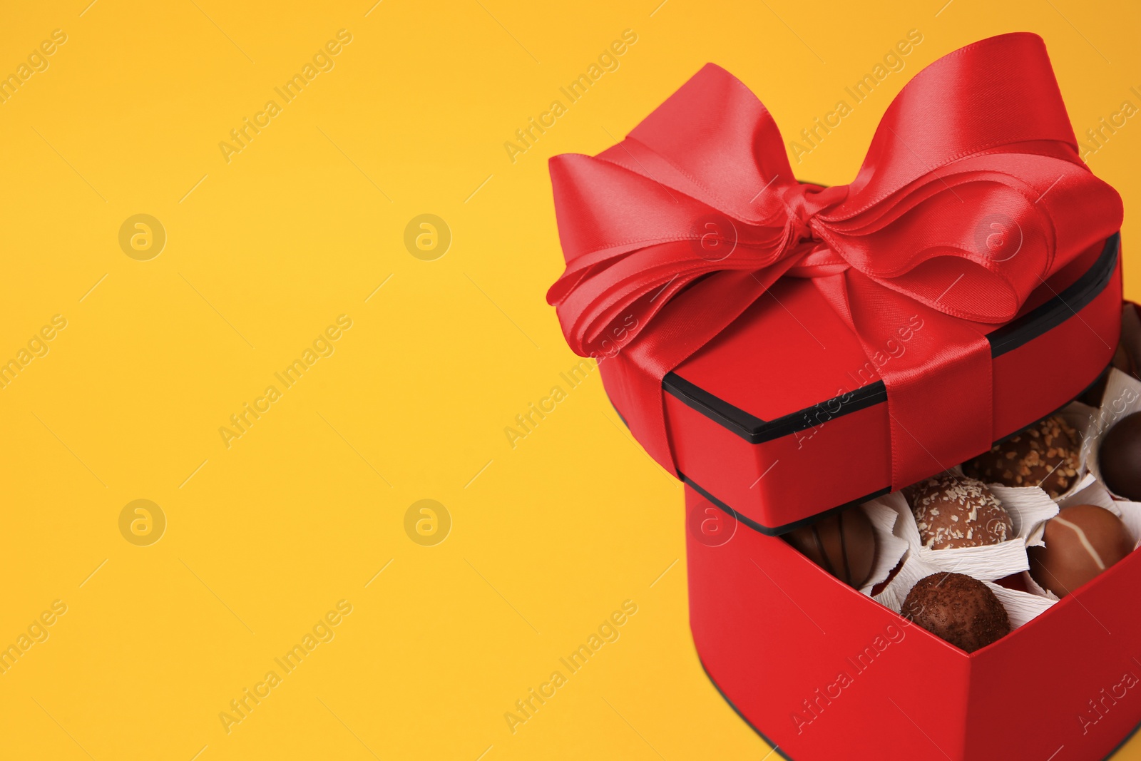 Photo of Heart shaped box with delicious chocolate candies on yellow background, closeup. Space for text