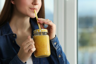 Photo of Beautiful young woman drinking delicious smoothie near window, closeup. Space for text