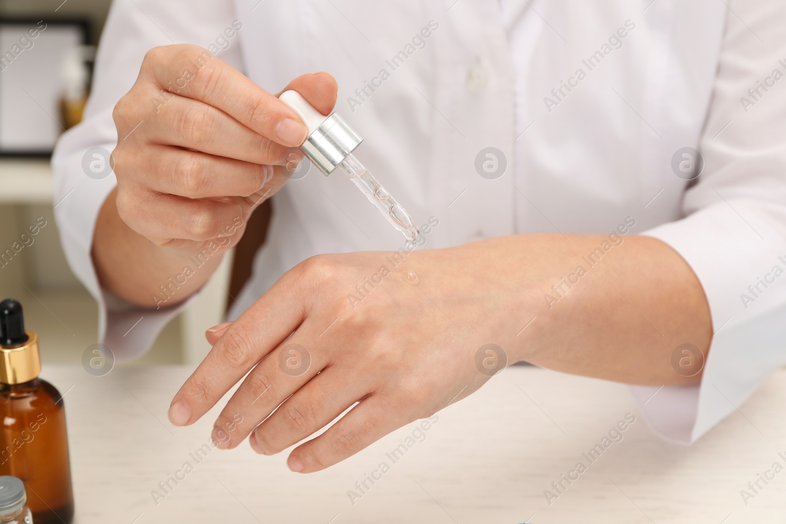 Photo of Dermatologist testing cosmetic product at white table, closeup