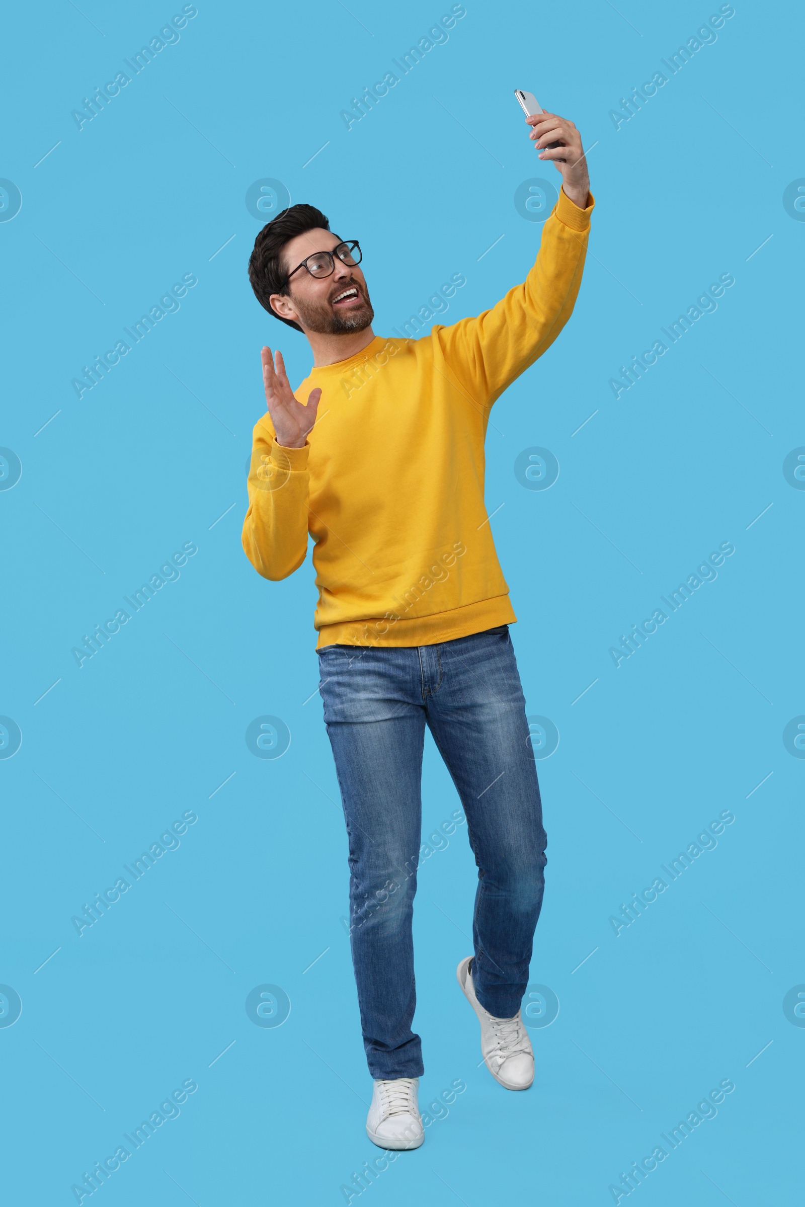 Photo of Smiling man taking selfie with smartphone on light blue background