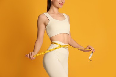 Photo of Happy woman in sportswear measuring waist with tape on yellow background, closeup
