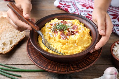 Woman eating banosh with brynza and pork cracklings at wooden table, closeup. Traditional Ukrainian dish