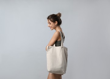 Happy young woman with blank eco friendly bag on light background