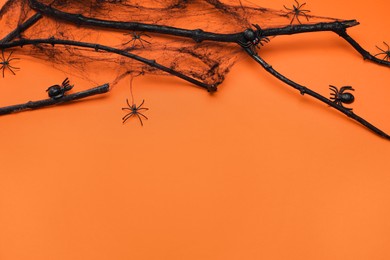 Photo of Black branches, spiders and space for text on orange background, above view. Halloween celebration