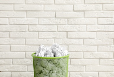 Photo of Metal bin with crumpled paper against brick wall, space for text