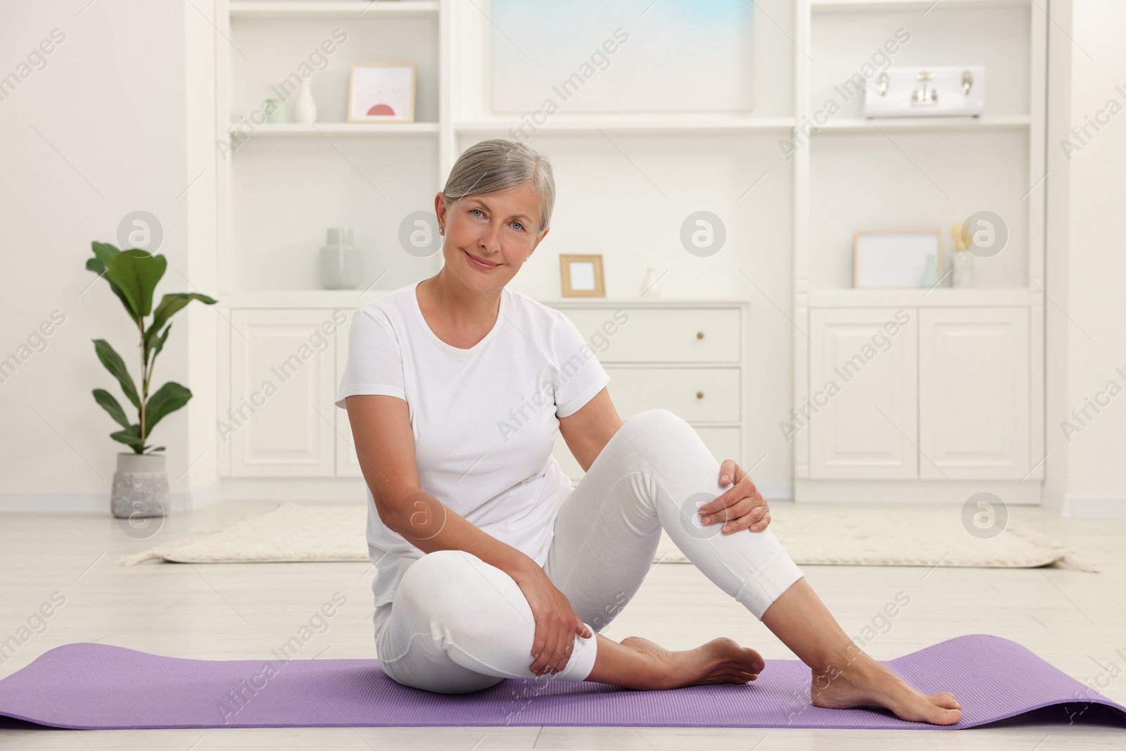 Photo of Happy senior woman sitting on mat at home. Yoga practice