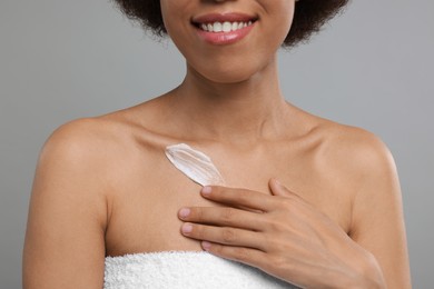 Photo of Young woman applying cream onto body on grey background, closeup