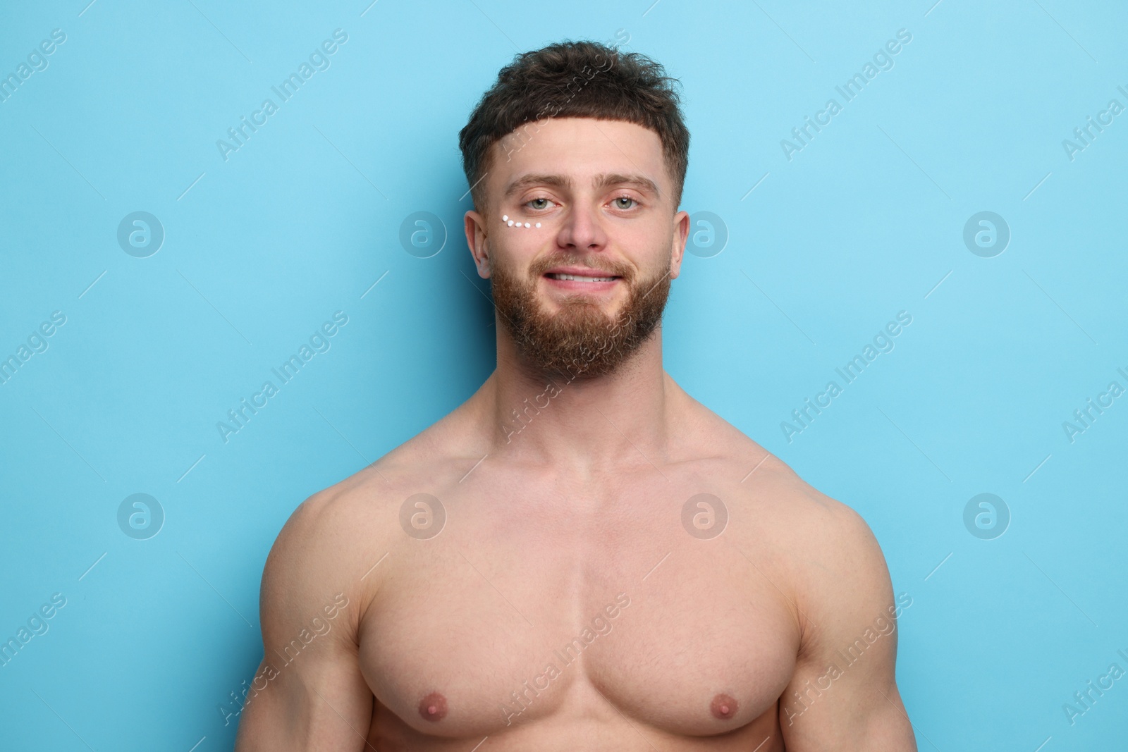 Photo of Handsome man with moisturizing cream on his face against light blue background